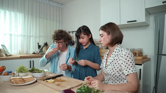 Happy caucasian father and mother sitting and eating fruit at modern kitchen. Energetic family spend time together by enjoy eating fruit or healthy fruit with kitchenware and fruit on table. Pedagogy.