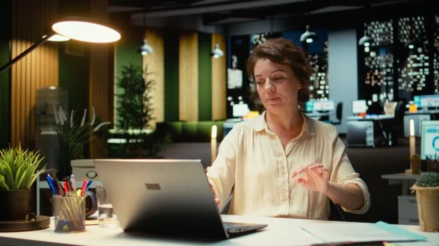 Businesswoman sits in a chair in a relaxed pose at midnight, daydreaming during a work break. Feels fulfilled and self assured, reflecting on her career success and corporate achievements. Camera A.