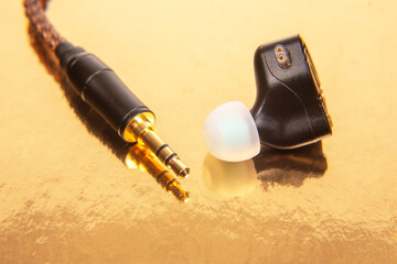 High-quality audio earbud with gold cable connection on reflective surface