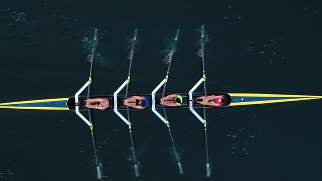 Top View Four Female Athletes Glide Gracefully In A Rowing Boat Across The Calm Ocean, Captured From Above As The Morning Sun Reflects On The Water Surface Creating A Magical Atmosphere.