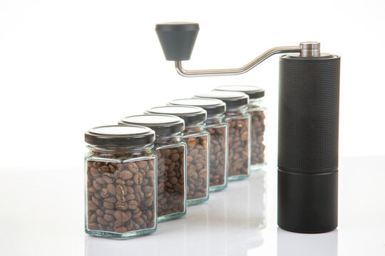 Coffee grinder next to jars of roasted coffee beans arranged on a white surface