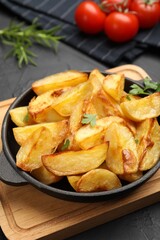 Tasty baked potatoes with parsley in frying pan on dark textured table, closeup