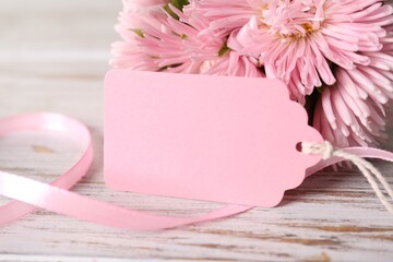 Blank card and flowers on white wooden desk, closeup. Space for text