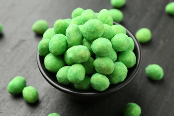 Delicious wasabi coated peanuts and bowl on dark textured table, closeup