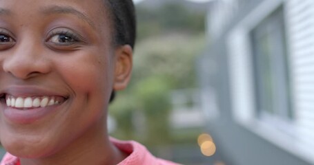 African American woman noticing camera and smiling on balcony in coral-pink sweatshirt, copy space - Powered by Adobe