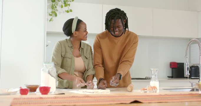 African American couple sprinkling flour then kneading dough at kitchen island for baking bread