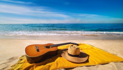 an acoustic guitar and straw hat resting on a yellow blanket on a sun drenched beach with blue ocean in the background summer vacation leisure concept