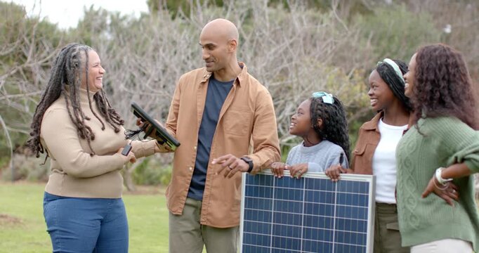 Diverse family walking into grassy clearing assembling compact solar panel while examining keys