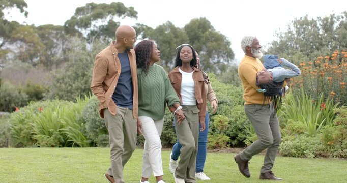 Diverse family walking in garden while grandfather pausing scoop child and parents gazing skyward