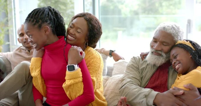 Camera panning revealing extended family laughing on gray sofa, older girl bursting forward