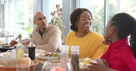 Diverse family starting breakfast at home table with mother leaning in asking daughter to try juice - Powered by Adobe