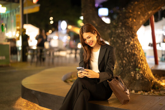Asian businesswoman smiling using smartphone in city night