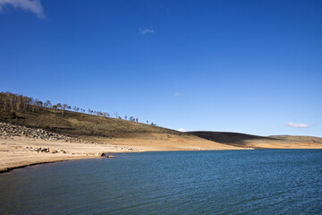 Tree-lined hills roll down to the clear waters of Lake Eucumbene in the Snowy Mountains of NSW, Australia. This alpine lake is regarded as a premier trout fishing location.