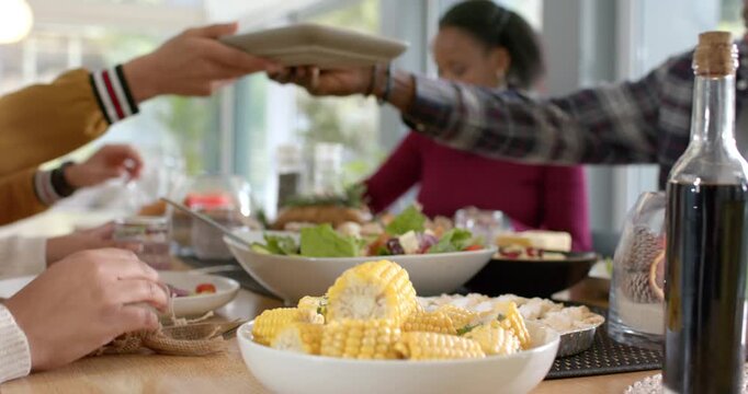 African American woman watching hands serving salad and corn at home while smiling receiving water