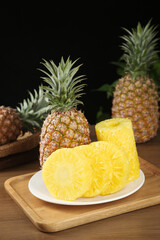 Fresh Golden Pineapple Slices on Plate with Whole Tropical Fruits on Wooden Board