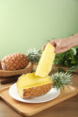 Fresh Golden Pineapple Slice Being Held by Hand on Wooden Board with Tropical Fruit