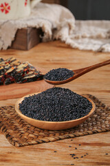 Black Sesame Seeds in Wooden Bowl and Spoon on Rustic Kitchen Table
