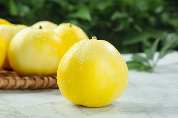 Fresh Golden Yellow Melons with Water Drops in Wicker Basket on White Wood Surface