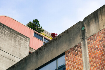 Low angle view of a concrete, red brick, and red-coated metal building exterior, with some balconies that have some plants just barely visible.
