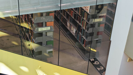 High angle view of nonfiction book stacks as seen through several panes of glass and partially hidden by a structural beam painted yellow.  