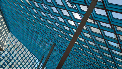 Low angle view of repeating pattern of windows along the large sloping surface of the roof with blue sky and sunlight visible. 