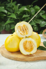 Fresh Sweet Yellow Melons Cut in Half on Wooden Board with Natural Green Background
