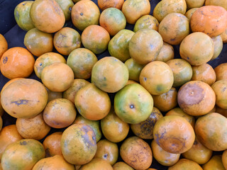 A large, unstructured pile of fresh oranges with a mix of yellow and greenish-orange peels, some showing slight blemishes. This abundant display of citrus fruit in a market or grocery store.