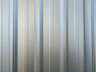 A corrugated galvanized steel surface, with a reflective, matte gray and silver finish. The texture features vertical ridges and subtle imperfections, creating an industrial, abstract background.