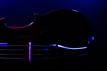 A violin on a dark background, side lit with purple and blue lights © MeganKobe