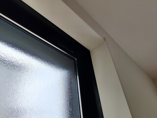 室内から見た白い壁と黒い窓枠およびすりガラスのサッシの一部を捉えた写真光の反射と質感の違いが抽象的な構成を生み出している