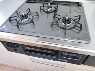 清潔なステンレス製のキッチンカウンターに設置された3口のガラストップガスコンロとその下にある魚焼きグリルを上方から捉えた写真