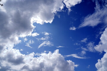 積雲や巻雲が青い空の周りを囲むように広がりその間から夏の強い日差しが降り注いでいる様子を捉えたダイナミックな空の写真