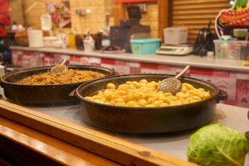 Fried potatoes and traditional stew cooking in large pans at Christmas market. Street food stall at festive fair at night. Concept of winter holidays in European city