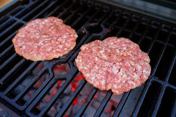 Two raw burger patties cooking on grill over glowing coals. Concept of barbecue, grilling and outdoor cooking