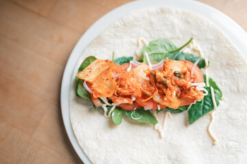 Open salad wrap in preparation with kimchi tomato, spinach, red onion and mayonnaise