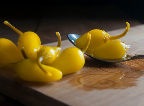 bodefgon fotografico. pepperoncini sobre una cuchara y sobre una tabla de cortar, en una mesa rusticaa de madera con fondo negro. Chile amarillo peque;o