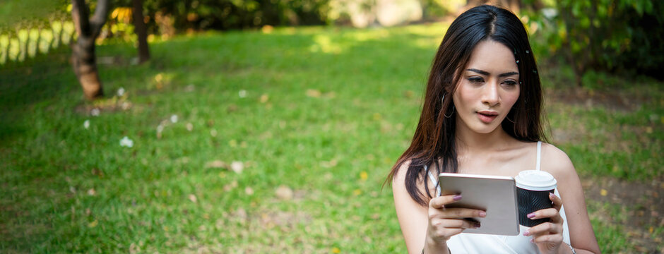 Banner asian woman sitting green garden park using phone listen music from smart phone with laptop computer. Panorama Happiness Woman toothy smile laughing happy working on laptop with copy space - Powered by Adobe
