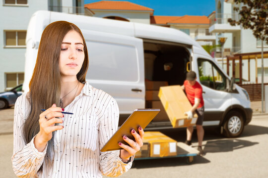 Woman manager of logistics company. Supervisor near courier. Delivery man unloads van. Courier takes boxes out of car. Woman manager controls logistics process. Transportation of goods