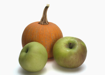 An orange pumpkin and two green apples centered on a white background.  There is ample room for text. The fresh produce is representative of fall harvest or autumn holidays. 