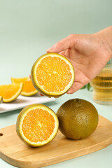 Hand holding fresh orange slice on wooden cutting board with citrus fruits in kitchen