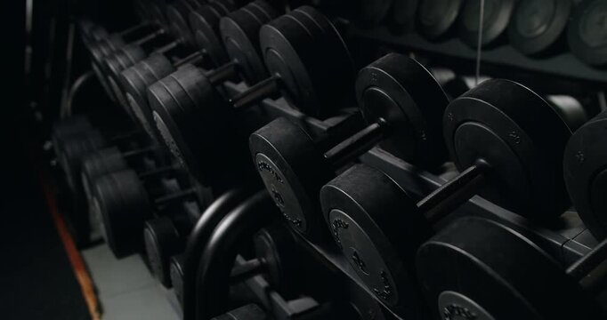 A detailed look at a rack of various weighted dumbbells in a professional gym setting, highlighting an atmosphere of strength training and fitness. Professional Fitness Gym Equipment Rack Filled