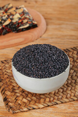 Black sesame seeds in white bowl with traditional grains on bamboo mat