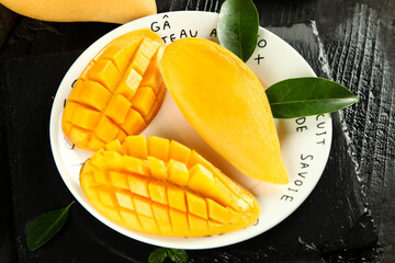 Fresh Ripe Mango Slices on White Plate with Green Leaves on Dark Wood Background