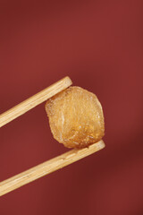 Dried Longan Fruit from Yunnan China Held in Chopsticks on Red Background - Traditional Asian Preserved Fruit Snack