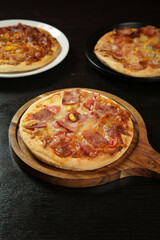 Fresh baked Italian pizzas with bacon and corn toppings on wooden serving board