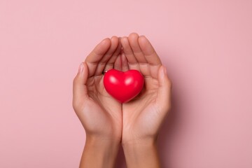 A delicate red heart held gently within outstretched hands against a soft pink backdrop evokes a sense of care and compassion.