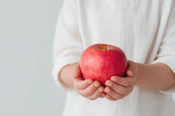 Fresh red apple held in hands against simple backdrop, symbolizi