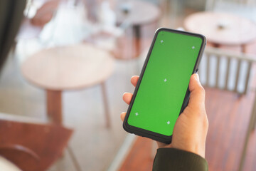 Person holding smartphone with green screen in cafe setting