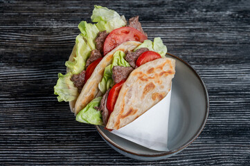 Homemade flatbread with beef and tomatoes on a table in a cafe. 