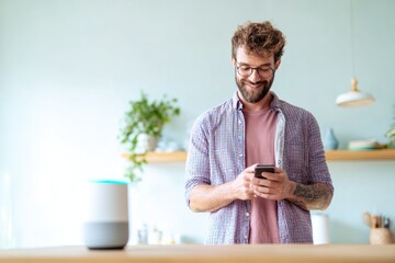 Smiling man interacts with smart speaker while using smartphone